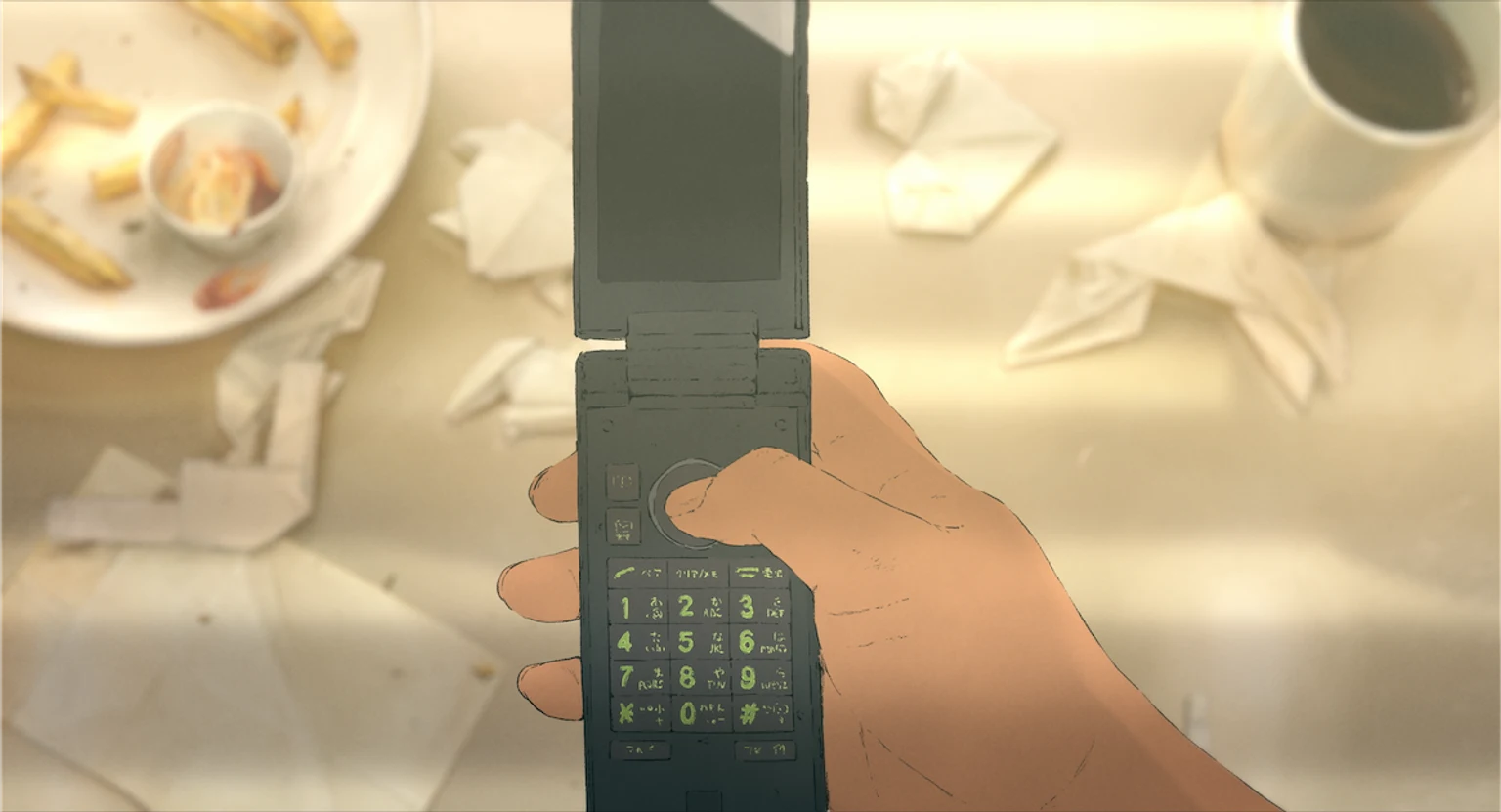 食卓の上で人の手が折りたたみ式携帯電話を操作する映画の場面画像。