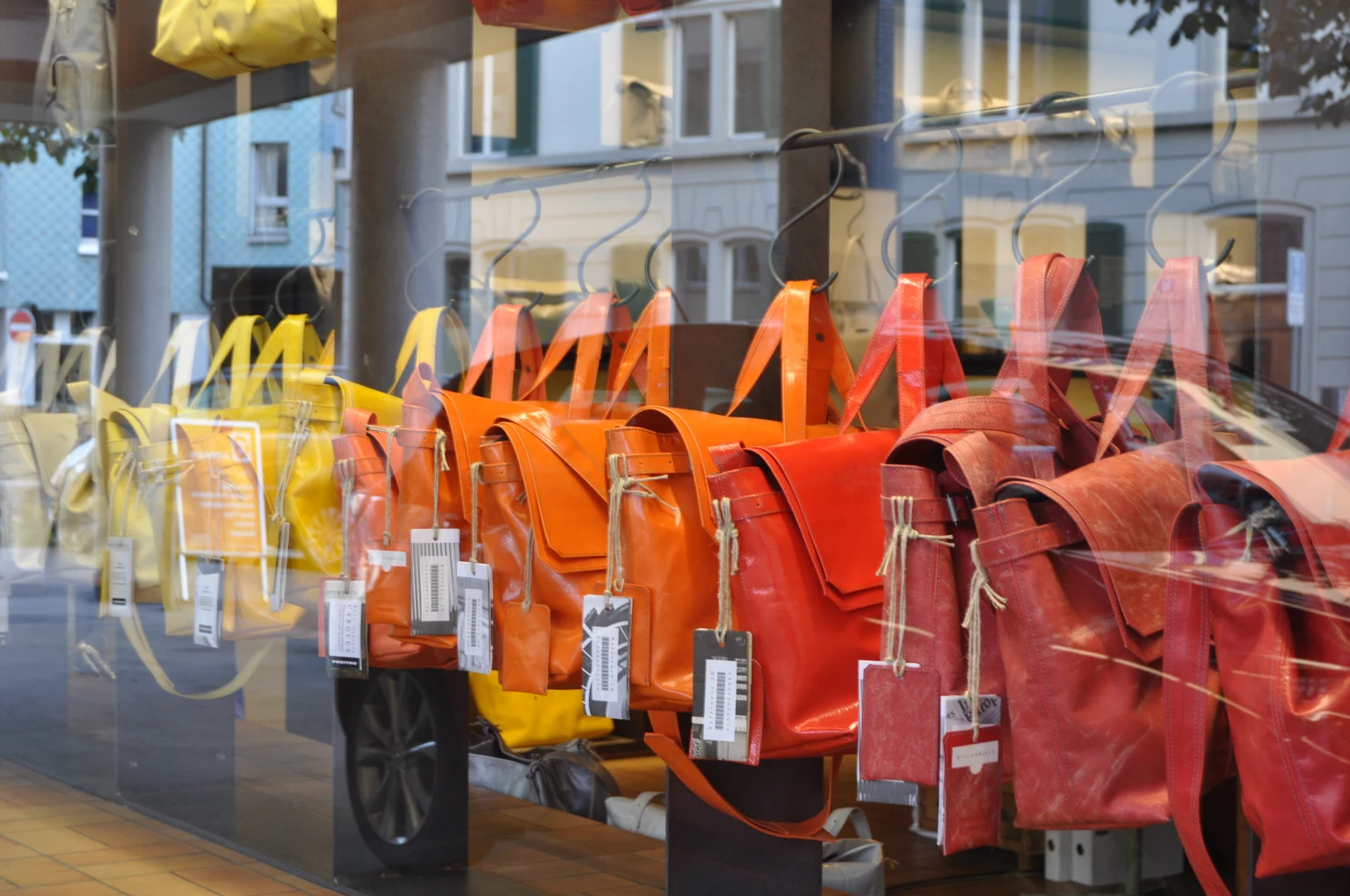 チューリヒのWerd店の窓越しに、黄色、オレンジ、赤のバッグと個別のタグが並ぶ