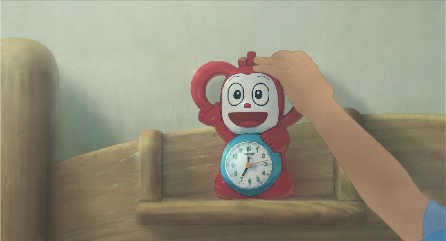 子どもの手が赤いキャラクターの目覚まし時計に触れている映画の場面画像。