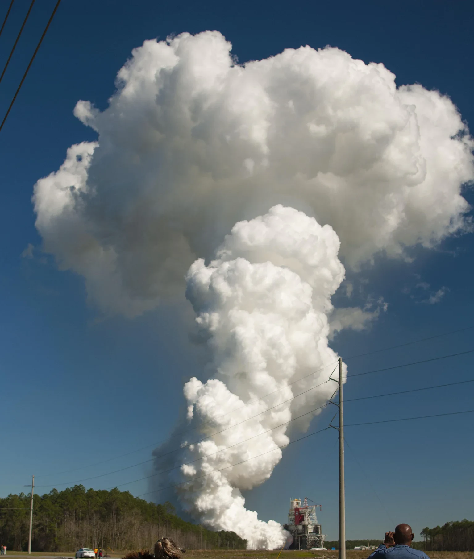青空の下、SLSコアステージのGreen Run hot fireで試験設備から大きな白い水蒸気雲が上がっている