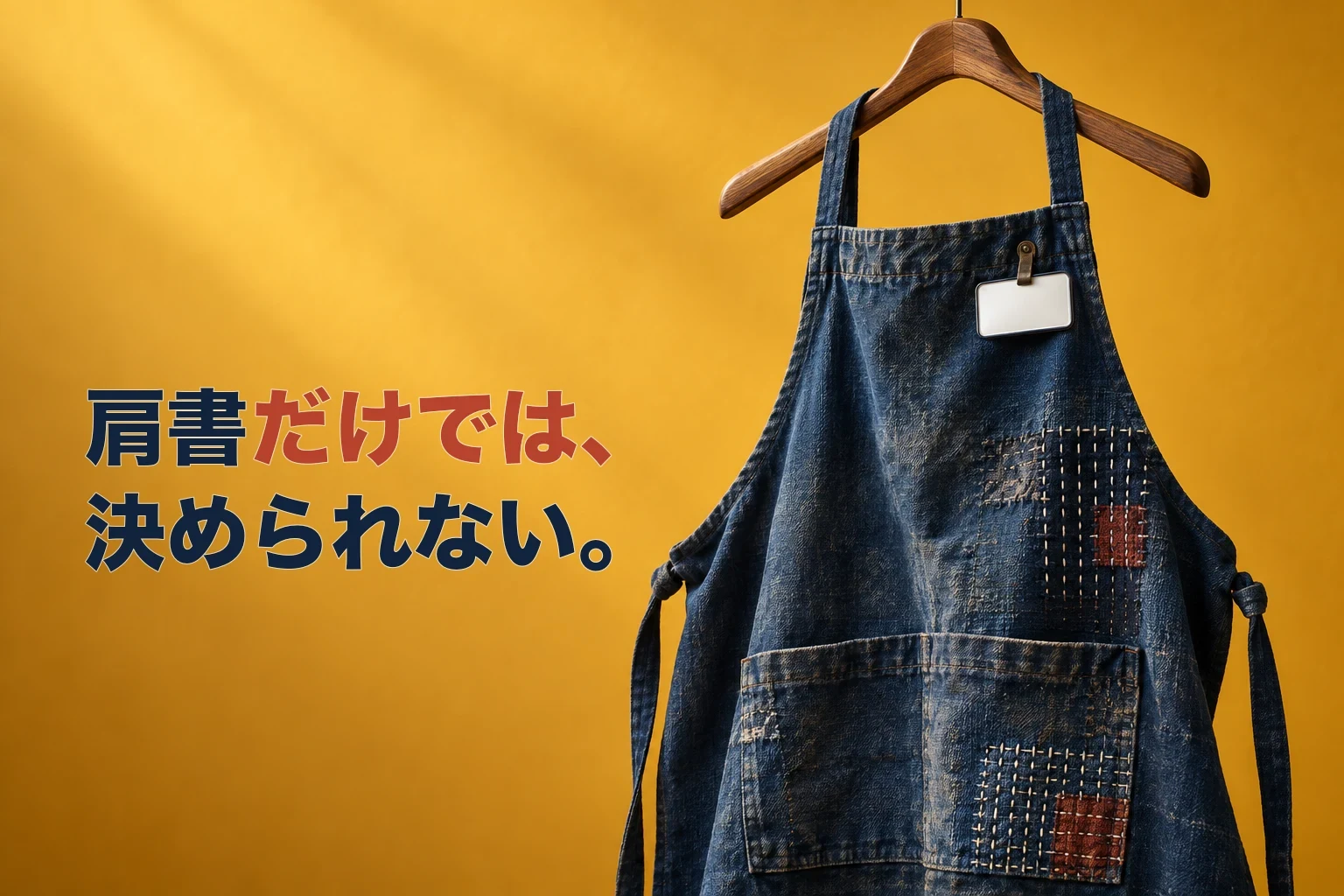 『肩書だけでは、決められない。』というコピーの横に、無地の白い名札を付けた使い込まれた藍色の仕事用エプロンを配した編集写真