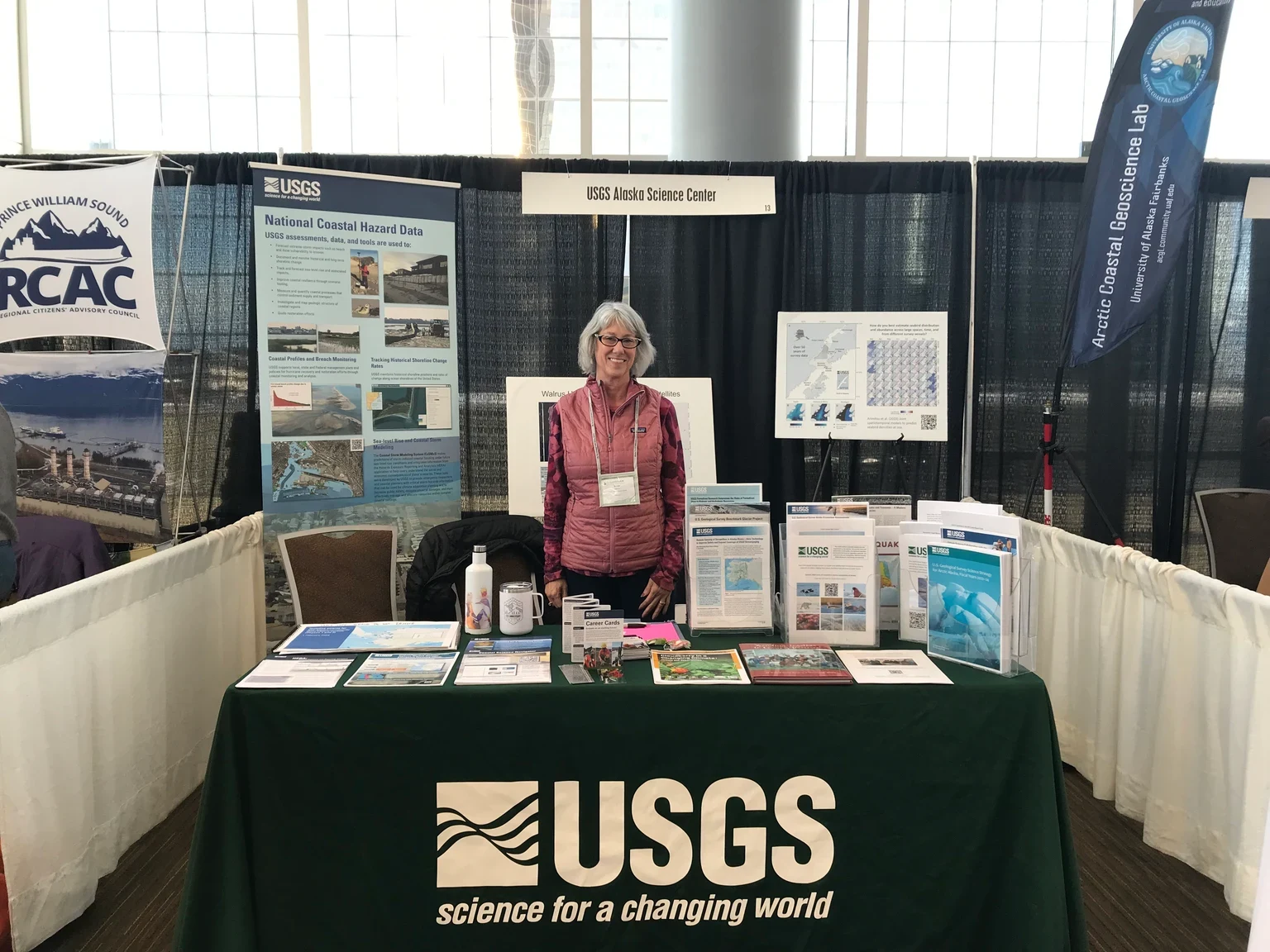 2024年Alaska Forum on the EnvironmentのUSGSブース。ポスター、資料、QRコード、担当者が配置されている