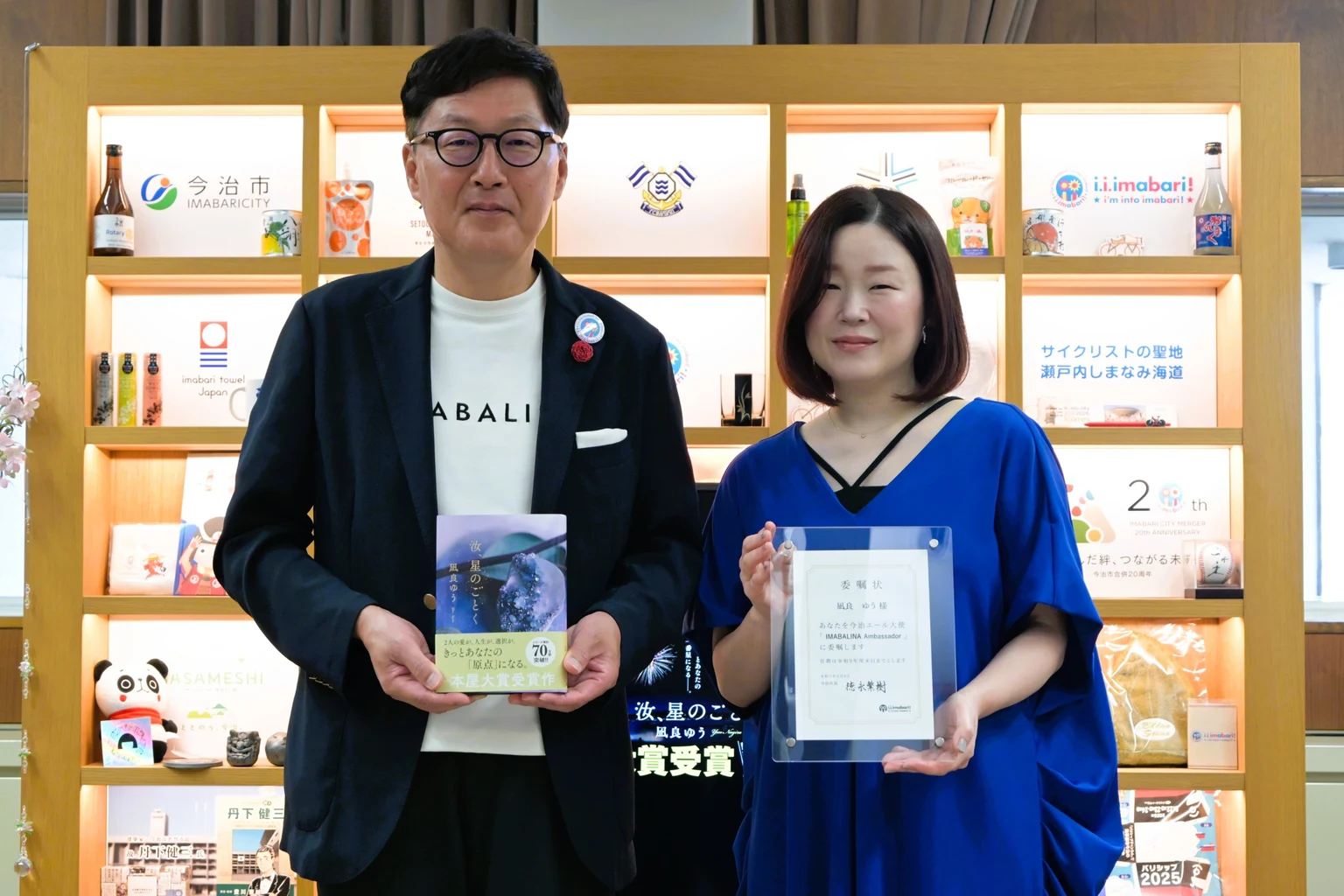 2025年8月4日の今治市の大使委嘱式。委嘱状を持つ凪良ゆうが右、著書を持つ徳永繁樹今治市長が左に立つ。