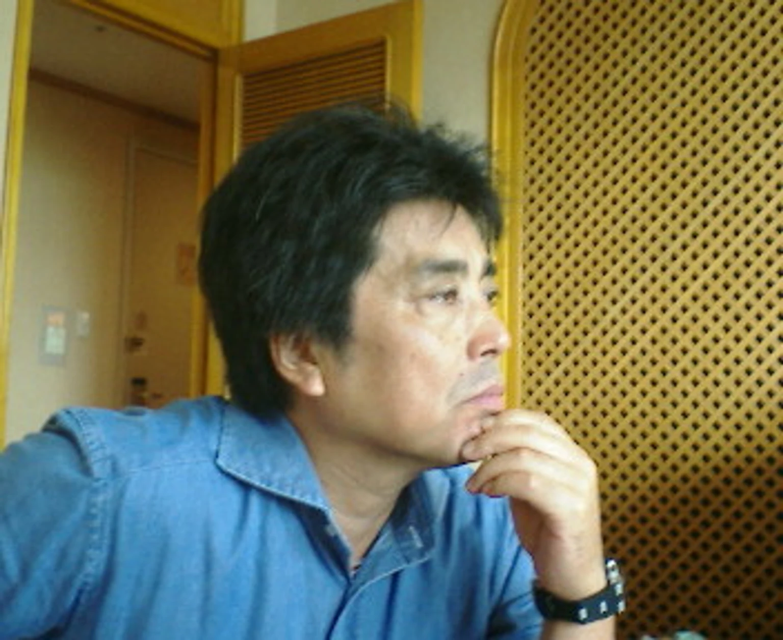 青いシャツを着て、手をあごに添えて座る村上龍。2005年6月3日撮影。